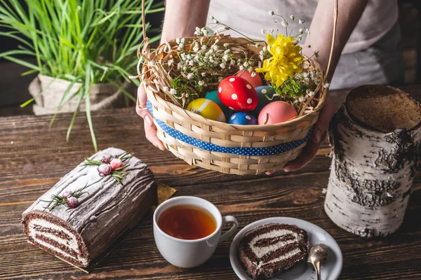 Almoço de Páscoa festivo com ovos brilhantes coloridos em uma cesta e um bolo em uma mesa de madeira. Férias tradicionais primavera . — Fotografia de Stock