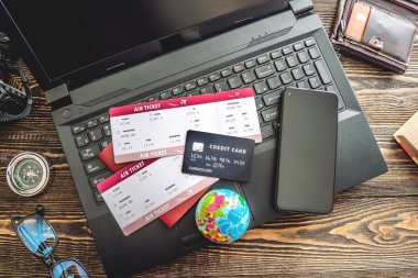 Heyecan verici bir yolculuğa hazırlanıyorum. Tahta bir arka planda dizüstü bilgisayar kullanarak uçuşları ayarlamak ve kredi kartıyla ödemek. Yukarıdan görünüşü.