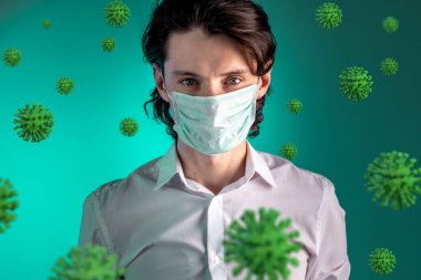 Yeşil arka planda COVIND-2019 Coronavirus ile çevrili tıbbi maskeli genç bir adamın portresi. 2020 'deki bir salgın ve salgın sırasında koruma ve tehdit.