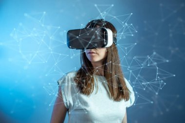 Sanal gerçeklik gözlüğü takan genç bir kadın gelecekçi tarzda mavi arka planda soyut çokgen bir ızgarada üç boyutlu görselleştirmeyi izliyor..