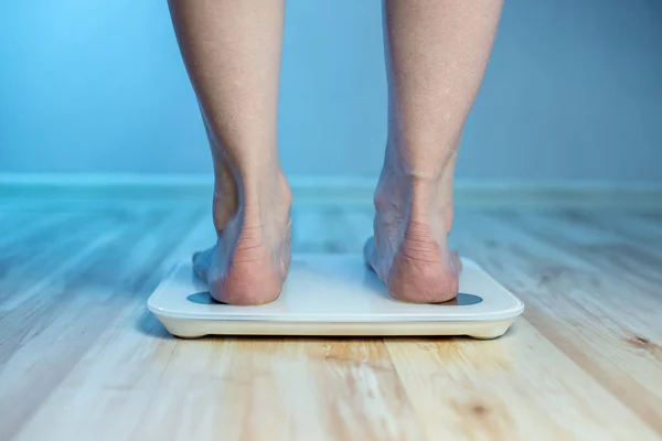 Women\'s bare feet stand on the floor electronic scales, to check the weight of the body and control the set of extra pounds in the blue light