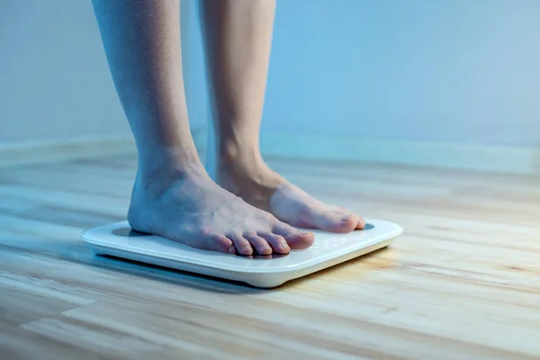 Women's bare feet stand on the floor electronic scales, to check the weight of the body and control the set of extra pounds in the blue light