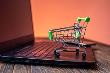 Kredi kartı olan bir alışveriş arabası mavi arka plandaki bir ekranın önünde dizüstü bilgisayarın üzerinde duruyor. Modern yaşamda internetten online alım kavramı