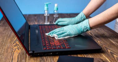 Steril eldivenli kadınların elleri iş yerlerinde dezenfektan laptopla peçete silerken kullanırlar. Virüslerle mücadelede temizlik ve hijyen