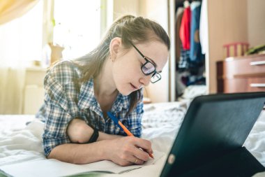 Genç bir kız öğrenci internette internetten ders veriyor. Evde, yatakta yatıyor. Covid-19 salgını sırasında okullarda ve üniversitelerde uzaktan eğitim