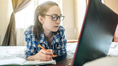 Genç bir kız öğrenci internette internetten ders veriyor. Evde, yatakta yatıyor. Covid-19 salgını sırasında okullarda ve üniversitelerde uzaktan eğitim