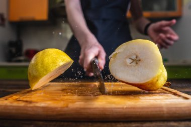 Şef, büyük bir bıçakla sarı olgun bir armudu ortadan ikiye ayırıyor. Su ve meyve suyu damlaları farklı yönlere uçar ve havada donar.