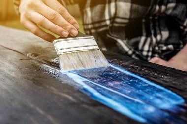 Bir marangoz şeffaf vernikten koruyucu bir tabaka uygular. Masanın üstüne yakın bir fırça ile el.