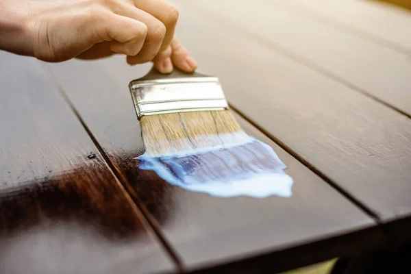 Bir marangoz şeffaf vernikten koruyucu bir tabaka uygular. Masanın üstüne yakın bir fırça ile el.