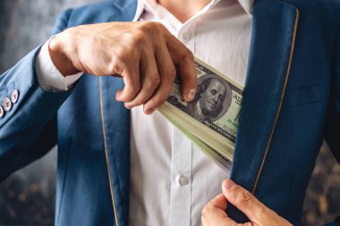 Takım elbiseli bir adam ceketinin iç cebine 100 dolarlık banknotlar koyuyor. Kapatın. Yolsuzluk ve rüşvet yetkilileri kavramı