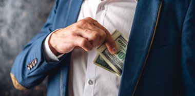 Takım elbiseli bir adam ceketinin iç cebine 100 dolarlık banknotlar koyuyor. Kapatın. Yolsuzluk ve rüşvet yetkilileri kavramı