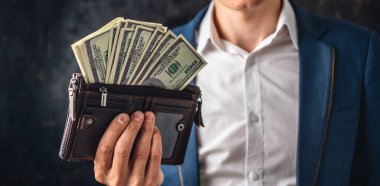 Takım elbiseli bir işadamı elinde bir yığın 100 dolarlık banknot tutuyor, gösterişli bir şekilde gösteriyor. Büyük miktarda para kazanma ve elde etme kavramı