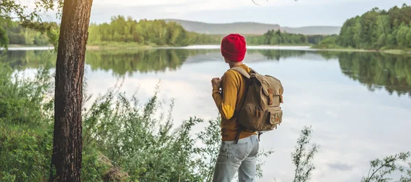 Турист Рюкзаком Красной Шапкой Стоит Реки Красивым Видом Воды Лесу — стоковое фото