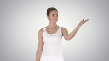 Boş tişörtlü bir kadın gradyan arkaplanda bir şeyin üzerinde yürüyor ve onu gösteriyor..