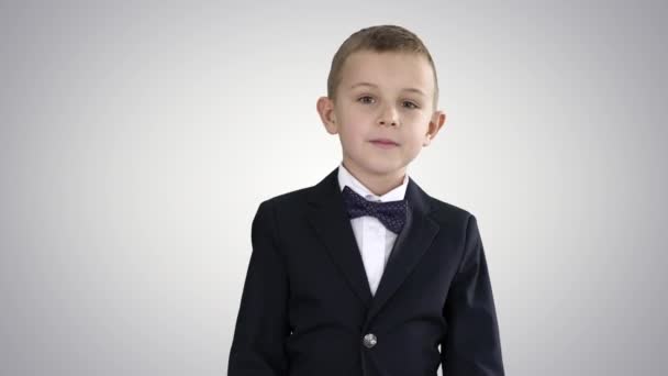 グラデーションの背景を歩く蝶ネクタイの衣装を着た小さな男の子. — ストック動画
