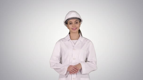 Зрелая инженер женщина в каске указывает на продукт или текст руками во время ходьбы по градиентному фону . — стоковое видео