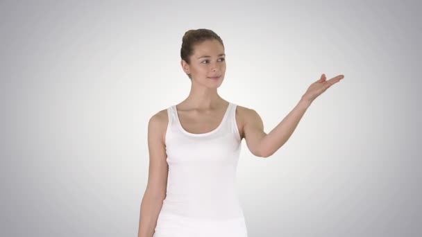Mujer en blanco gradiente camiseta sin mangas caminando y mostrando en algo a un lado en el fondo gradiente. — Vídeo de stock