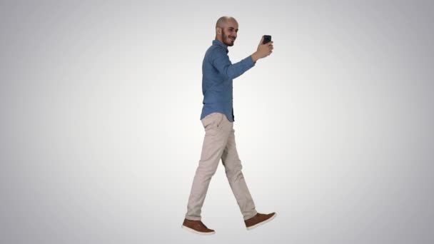 Feliz joven guapo sonriente haciendo selfie mientras camina sobre fondo degradado . — Vídeos de Stock