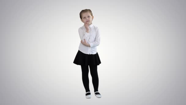 A curious little girl stands and thinks on gradient background. — Stockvideo