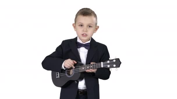 Menino em um traje andando e jogando ukulele no fundo branco . — Vídeo de Stock