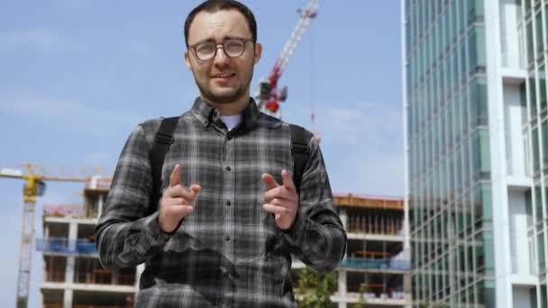 Slimme casual man in bril praten met camera met bouwplaats op de achtergrond. — Stockvideo