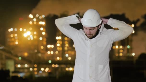 Ingénieur redresse les vêtements et regarde la caméra debout près de la raffinerie de pétrole . — Video