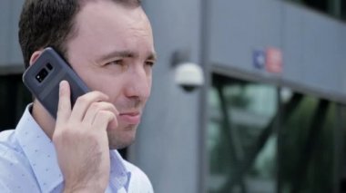 Yakışıklı adam telefonla konuşuyor ve modern binanın arka planında yürüyor..
