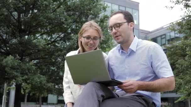 Zakelijke vrienden werken aan een laptop in het park vlakbij het kantoorgebouw. — Stockvideo