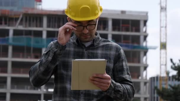 Un trabajador cansado con la tableta en un sitio de construcción . — Vídeos de Stock