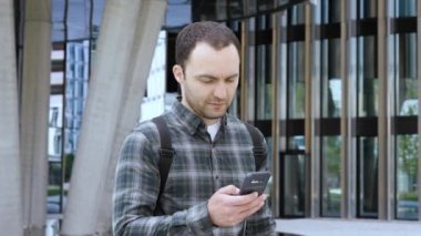 Modern Bina 'nın yakınında yürüyen sıradan bir adam ve akıllı telefon tebessümü kullanıyor..