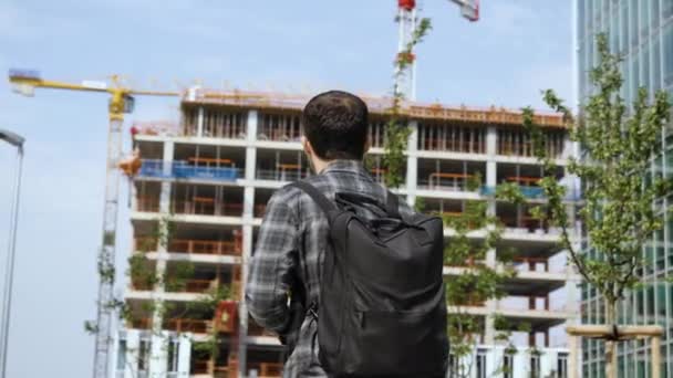 Schöner Mann mit Rucksack läuft auf Baustelle zu. — Stockvideo