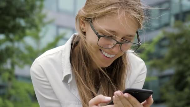 Młoda uśmiechnięta kobieta korzystająca z telefonu na zewnątrz. — Wideo stockowe