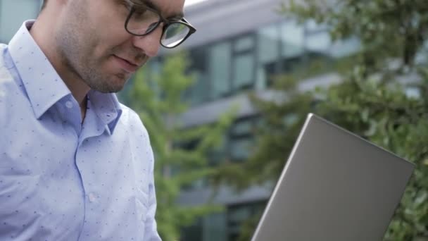 Ottimo risultato. Giovane bell'uomo che usa il computer portatile seduto su una panchina in un parco . — Video Stock