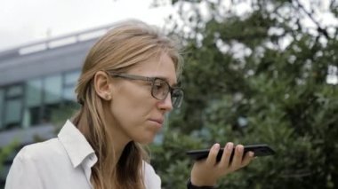 Gözlüklü bir kadın dışarıda akıllı telefon ses tanıma özelliği kullanıyor..