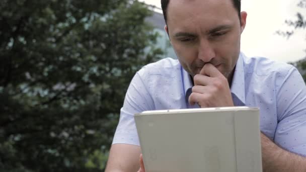 Knappe man werkt met tablet in het park. — Stockvideo