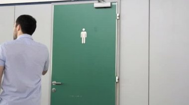 Adam kapıyı açıyor ve erkekler tuvaletine giriyor..