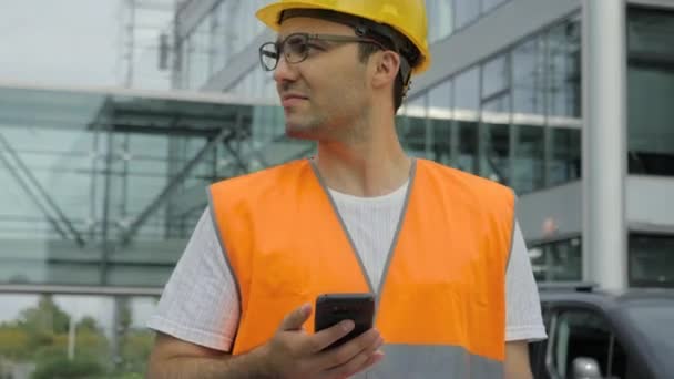 Jovem engenheiro esperando que alguém venha, olhando para o telefone e fazendo uma chamada . — Vídeo de Stock