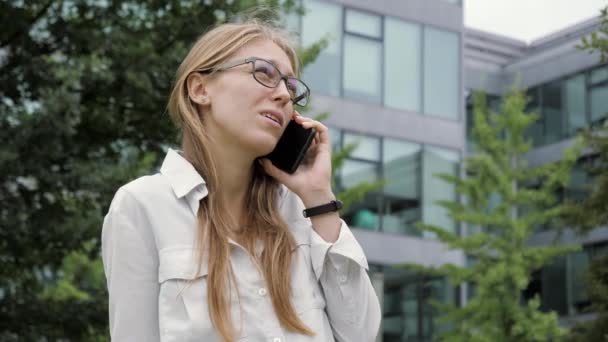 Mujer de negocios con cabello rubio en gafas haciendo una llamada por el edificio de oficinas . — Vídeos de Stock