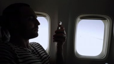 Uçakta oturmuş telefonundaki fotoğraflara bakan bir adam..
