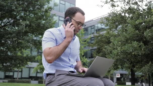 Podnikatel pracující venku v parku, pomocí notebooku a mluvení na mobilu. — Stock video