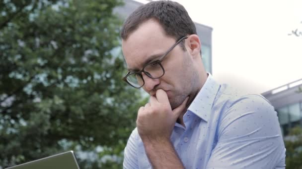 Guapo joven hombre de negocios utilizando un ordenador portátil sentado pensando y reaing . — Vídeo de stock