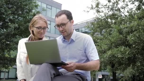 Navigare in rete insieme. colleghi di lavoro seduti sulla panchina insieme e guardando il computer portatile . — Video Stock