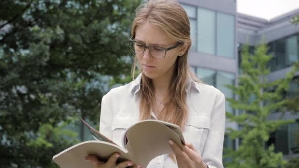 Beautiful smart woman reading magazine in the park. — Stok video