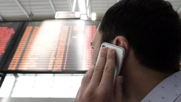 Homem a olhar para o horário da companhia aérea e a falar ao telefone . — Vídeo de Stock