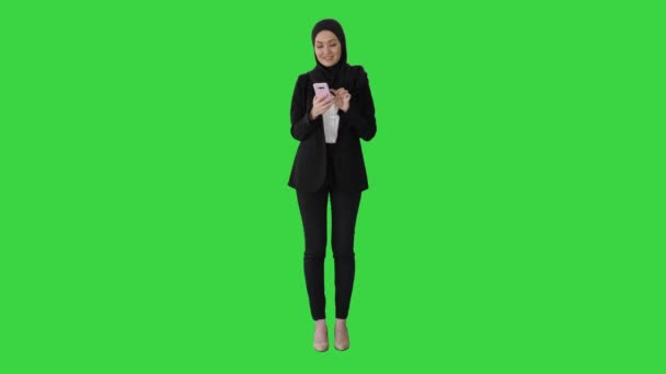 Молода жінка-муслім, одягнена в хіджабський хустку, яка ходить за допомогою смартфона на зеленому екрані, Chroma Key. — стокове відео