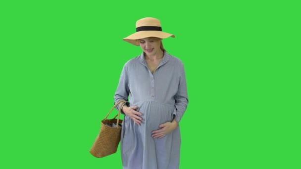 Schöne schwangere Frau in Sommerkleidung mit Hut, der ihren Bauch auf einem Green Screen berührt, Chroma Key. — Stockvideo