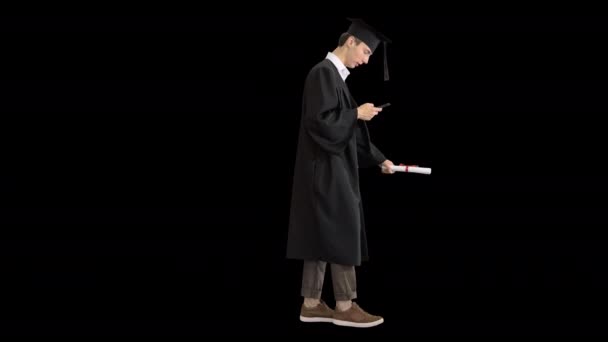 Graduación: Estudiante feliz caminando y mensajes de texto en su teléfono, Alpha Channel — Vídeo de stock