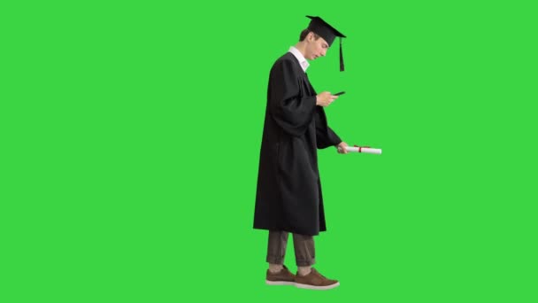 Graduazione: Felice studente a piedi e sms sul suo telefono su uno schermo verde, Chroma Key . — Video Stock