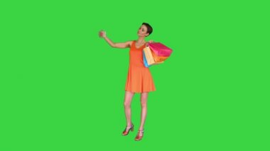 Çekici genç bir kadın elinde farklı boş alışveriş torbalarıyla yeşil ekranda selfie çekiyor, Chroma Key..