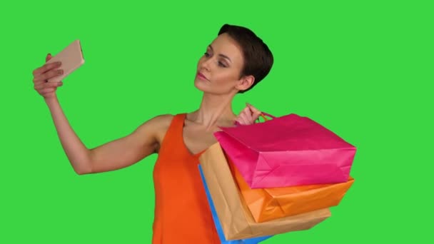 Ελκυστική νεαρή γυναίκα κρατώντας διαφορετικές κενές τσάντες ψώνια κάνοντας selfie σε μια πράσινη οθόνη, Chroma Key. — Αρχείο Βίντεο